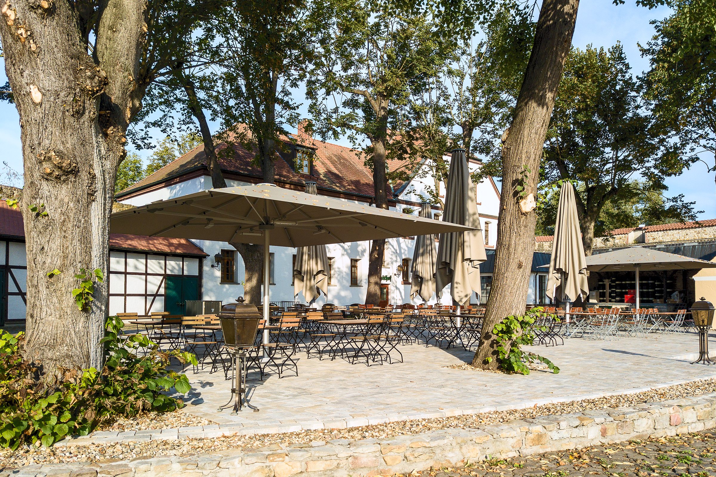 Biergarten der Wasserburg Gommern mit Sitzplätzen und Sonnenschirmen unter alten Bäumen